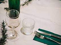 Tischgedeck mit grünen Wasserflaschen, einem Wein- und einem Wasserglas und grünen Zweigen als Dekoration.