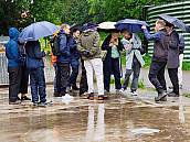 Bild von den Besucher bei Regen auf einem Platz vor dem Hof. Mit Regenschirmen und/oder Regenbekleidung